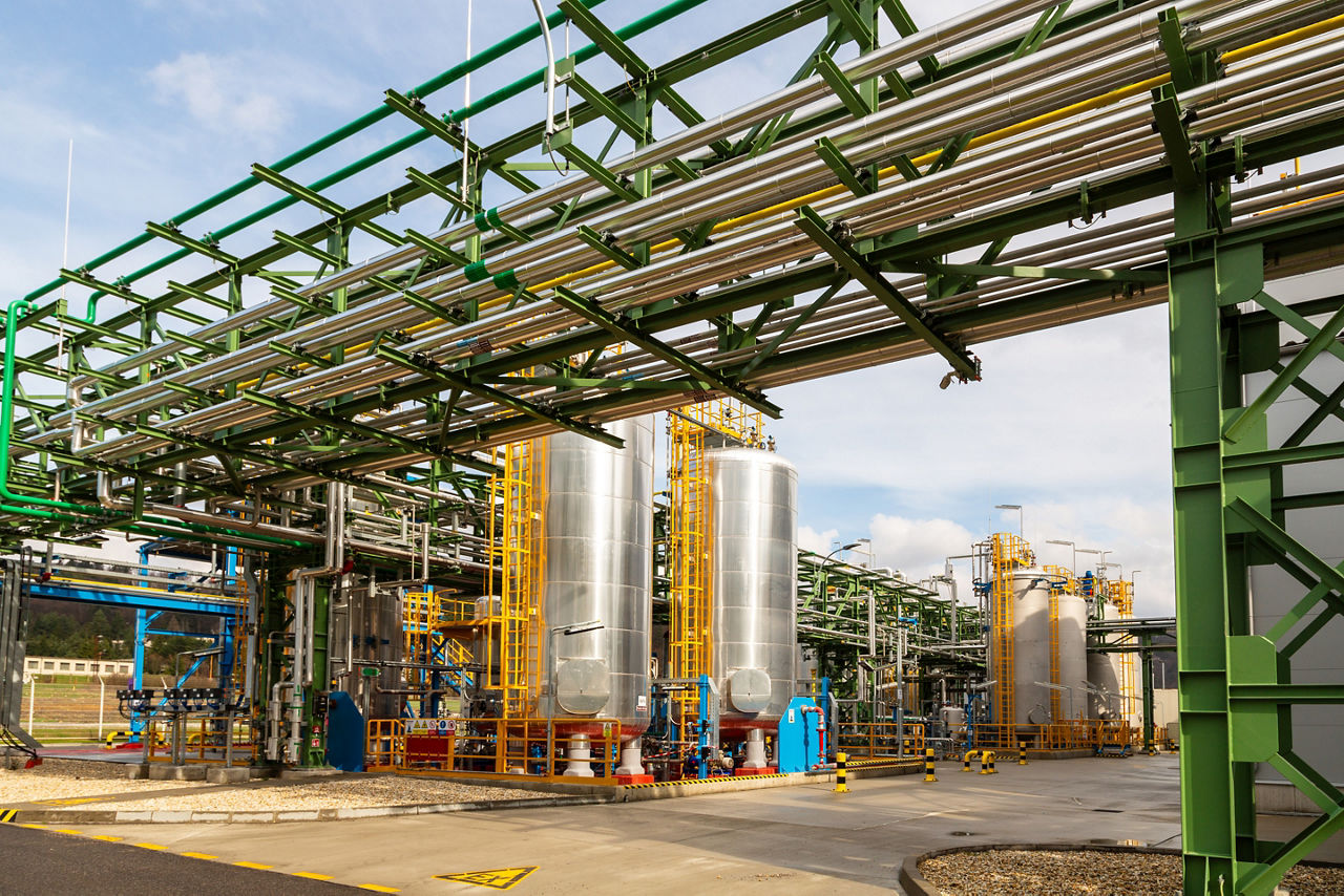 Zwei große silberne Produktionskessel, davor laufen oben quer einige Rohre durch eine Rohrbrücke.