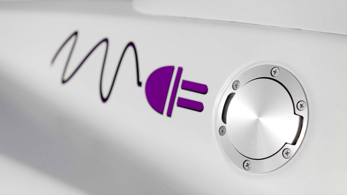 Close-up of a metallic circular fuel cap on a white surface with a purple electric plug symbol.