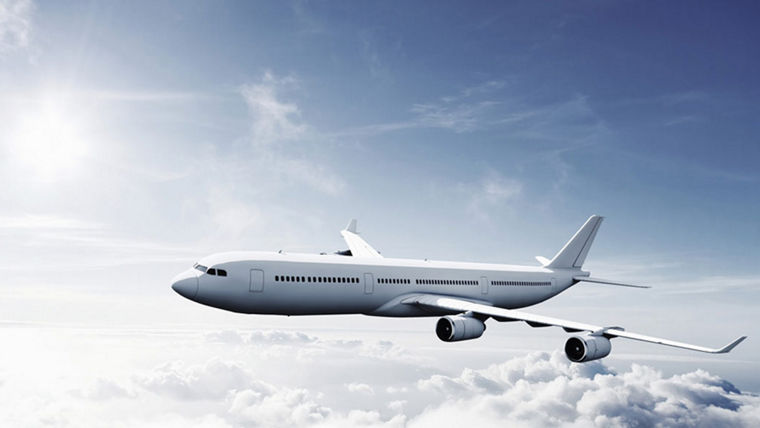 A large commercial airplane flying above clouds under a bright sun and clear sky.