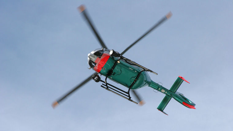 Helicopter with green and red body flying against a clear blue sky.