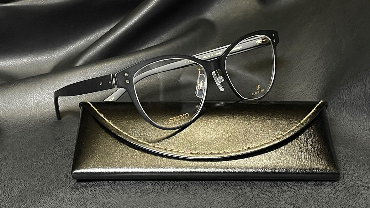 Black-framed eyeglasses resting on a matching black leather case with visible stitching.