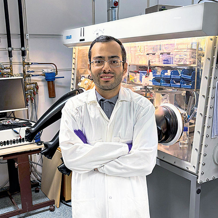 Saeed Mardi steht mit verschränkten Armen, Laborkittel, Handschuhen und Schutzbrille in einem Chemielabor.