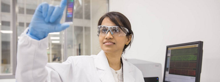 A lab technician in a white coat holds a colorful gel, analyzing results in a modern laboratory setting.