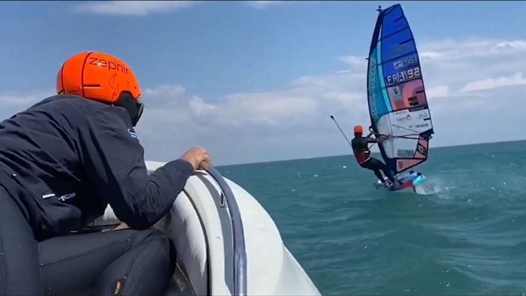 EIn Windwurfer fährt in hohem Tempo, gefolgt von einem motorisierten Schlauchboot.