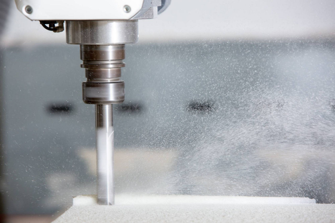 Close-up of a milling machine cutting a white material with dust particles dispersing.