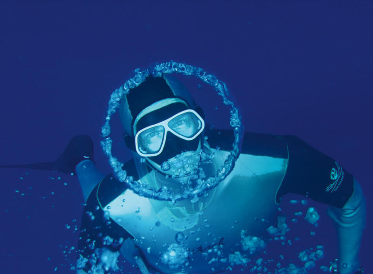 Herbert Nitsch taucht und blickt in die Kamera. Um sein Gesicht ist eine kreisförmige Luftblase.