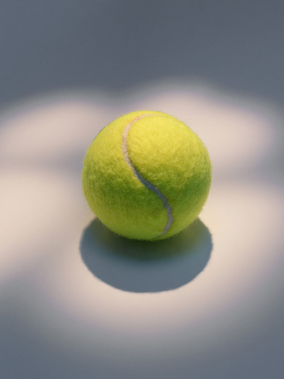 A yellow tennis ball lies on an illuminated surface.