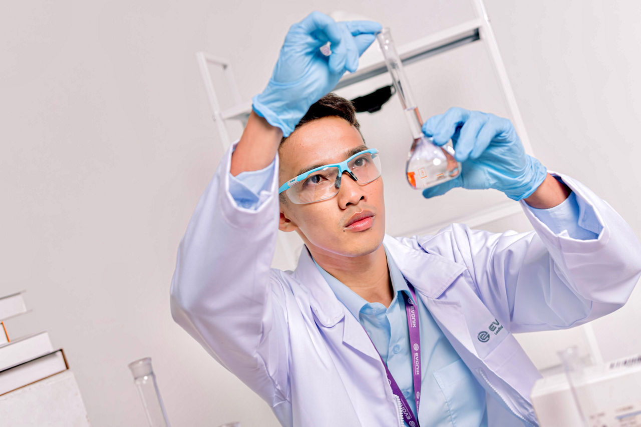 Scientist wearing blue gloves and a white lab coat holding a flask with orange liquid.