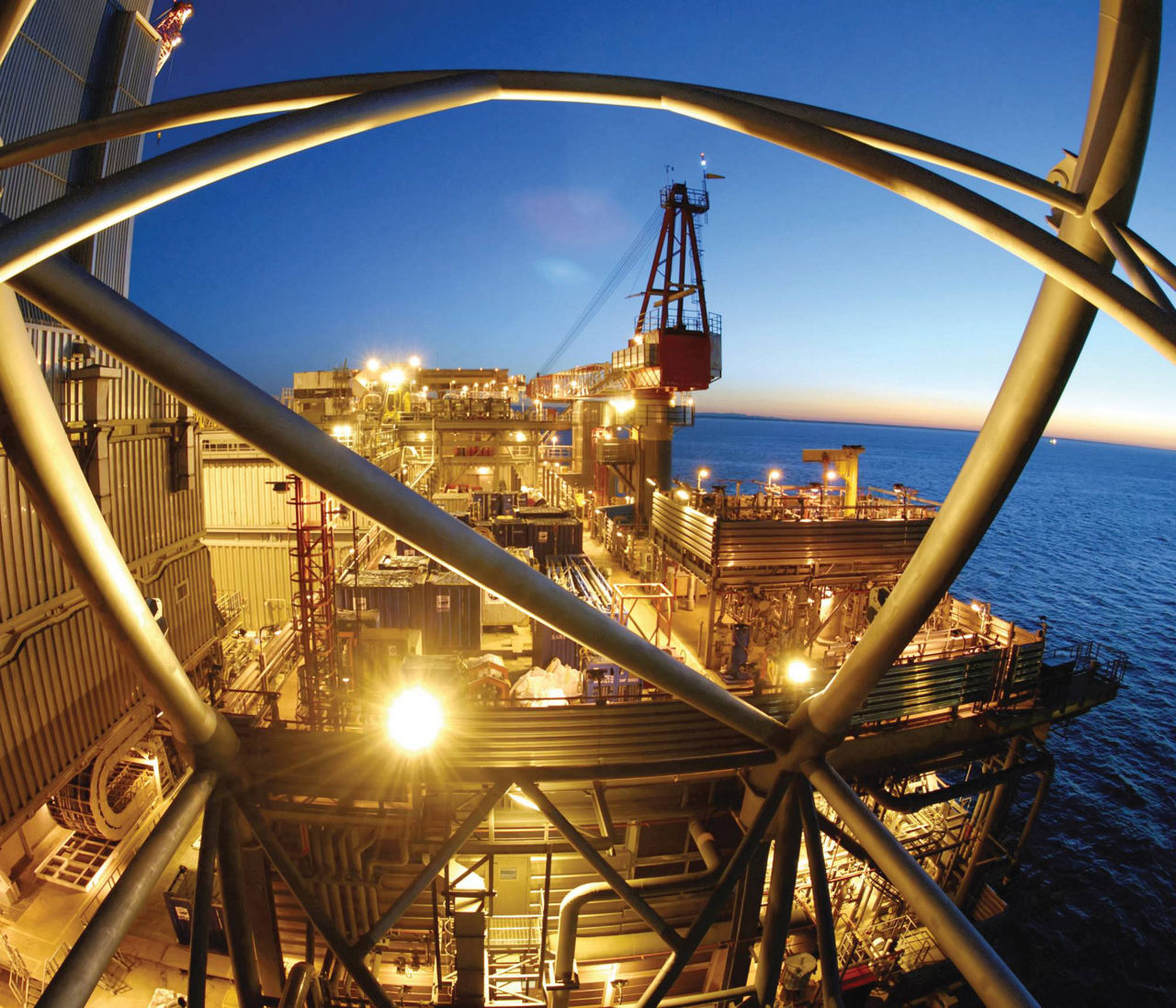 Offshore oil platform illuminated at dusk with structural beams in the foreground.
