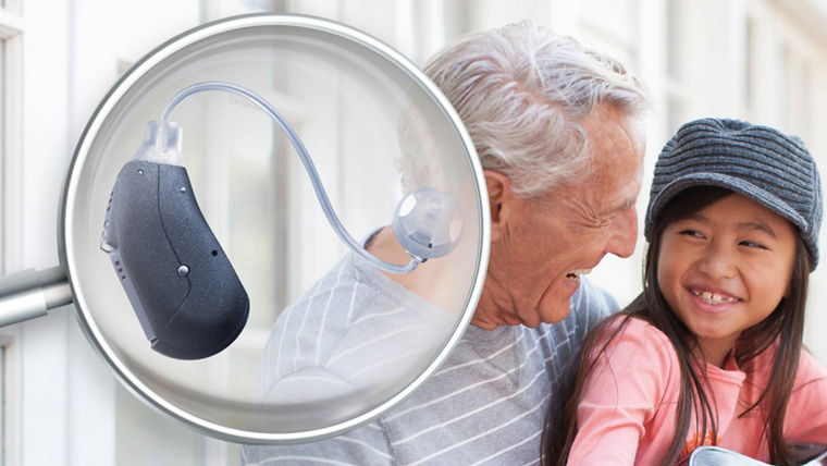 Magnified hearing aid device with an elderly person and child in the background.