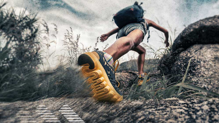 A person hiking uphill wearing yellow-soled shoes and a backpack on rocky terrain.