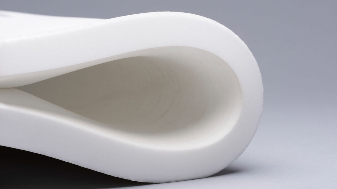 Close-up of a rolled white foam sheet with a smooth texture against a gray background.