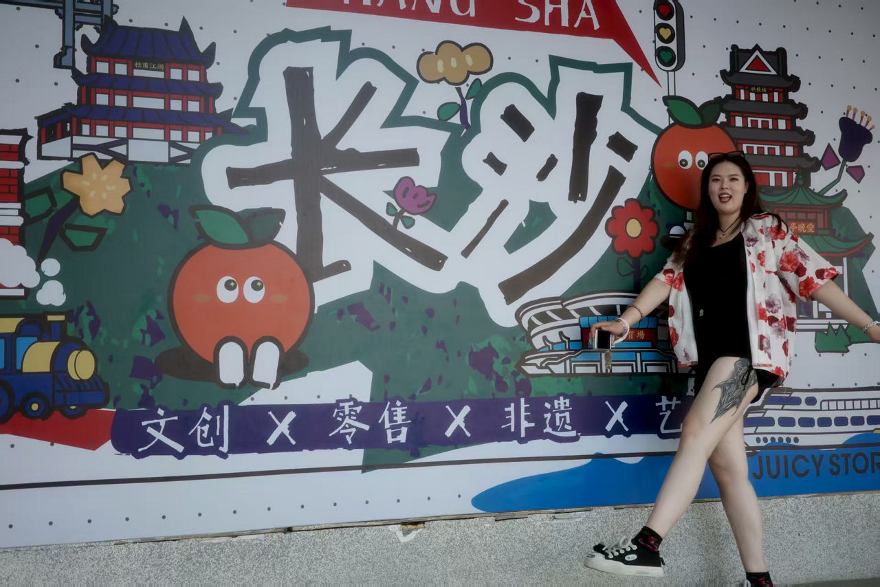 A person poses in front of a colorful mural featuring the name "Changsha" and playful illustrations.