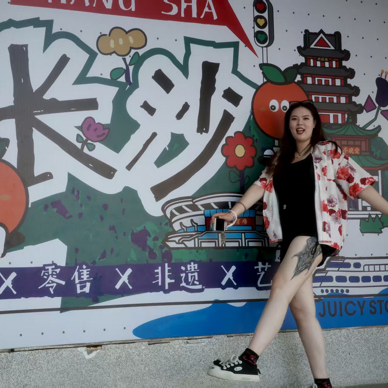 Eine Person posiert vor einem bunten Wandgemälde mit dem Schriftzug "Changsha" und verschiedenen Illustrationen.