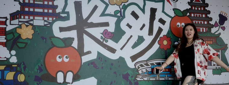 Eine Person posiert vor einem bunten Wandgemälde mit dem Schriftzug "Changsha" und verschiedenen Illustrationen.