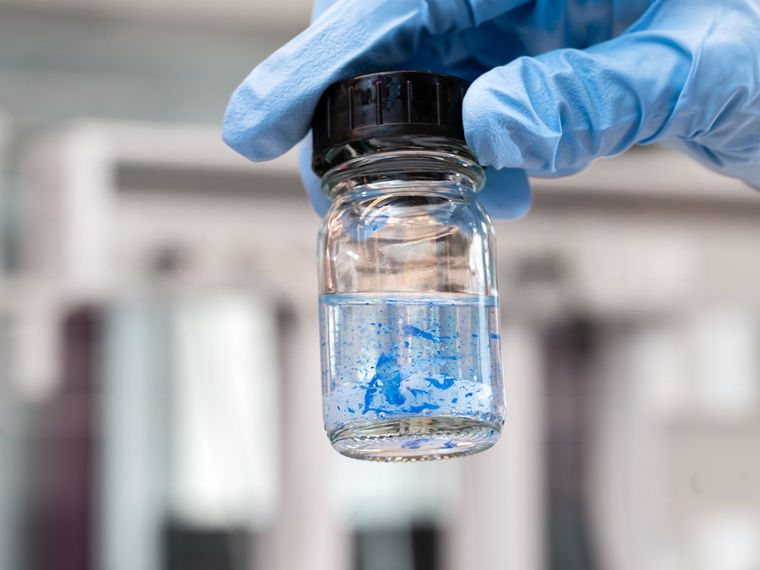A gloved hand holds a sample vial in which ink is separating from plastic particles.