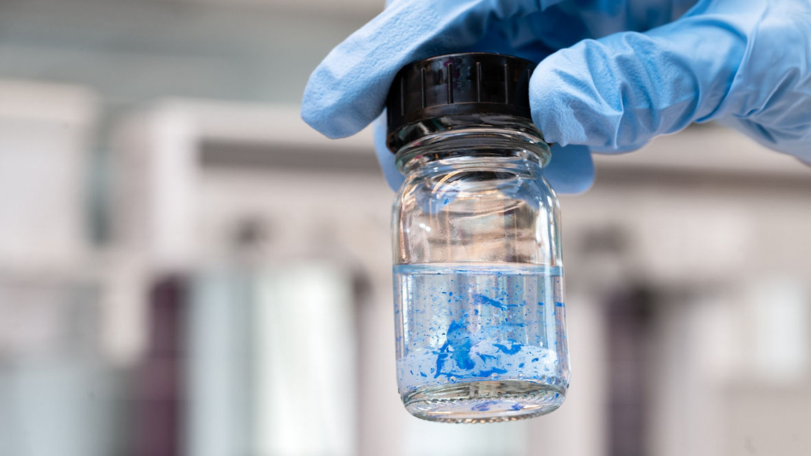 A gloved hand holds a sample vial in which ink is separating from plastic particles.