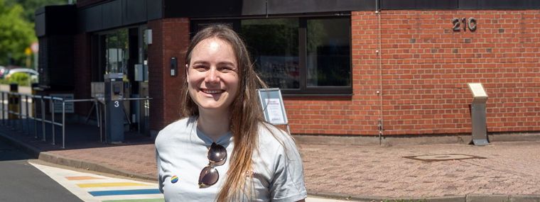 A smiling woman stands near a colorful striped crosswalk in front of a brick building.