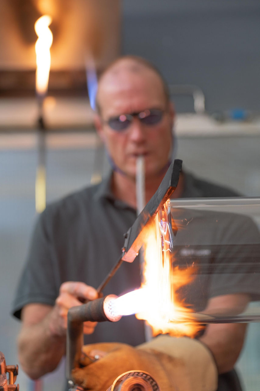 Udo Musholt erhitzt einen Glaskörper über eine großen, gelblichen Flamme.