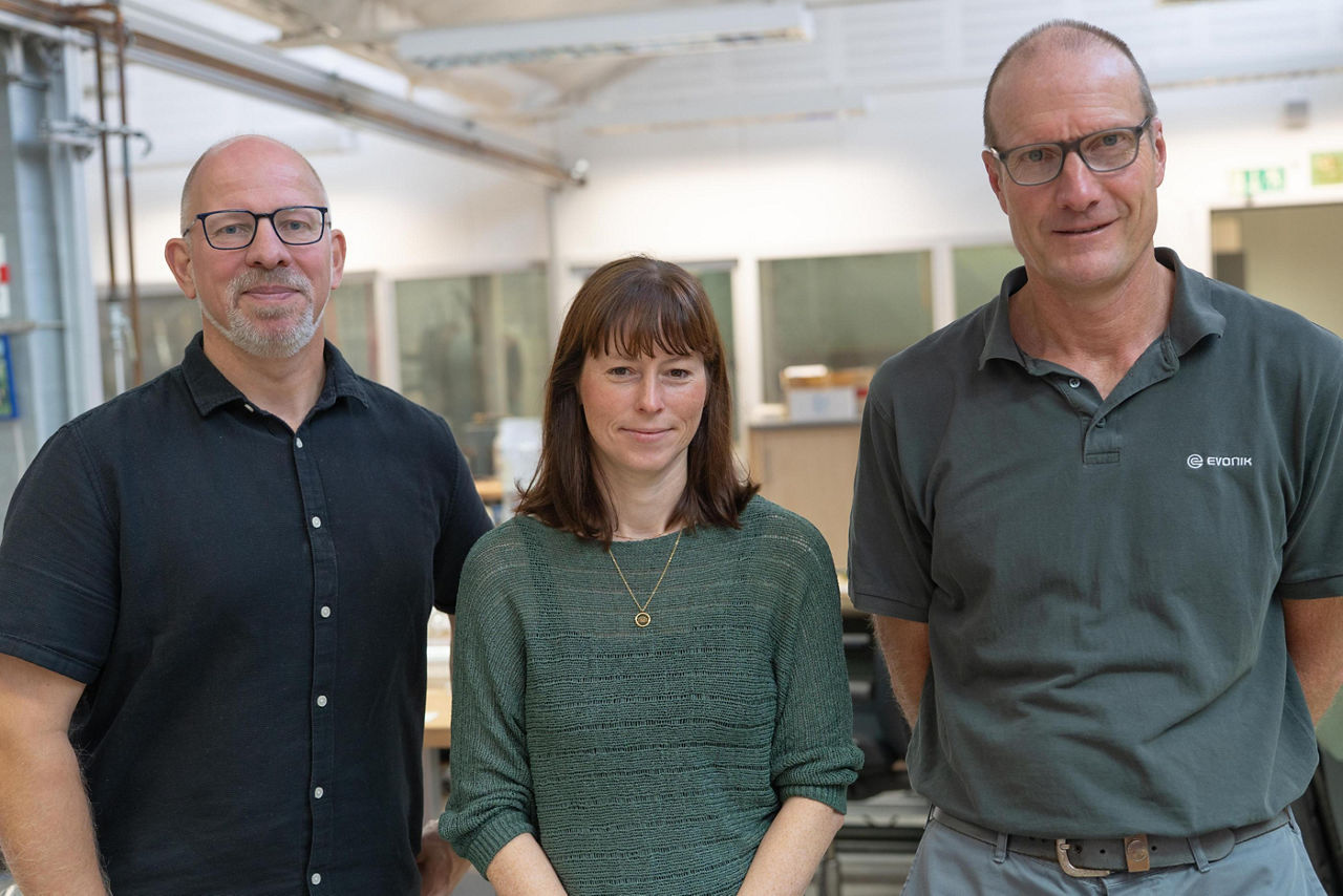 Drei Personen in der Glasbläserei schauen in die Kamera.