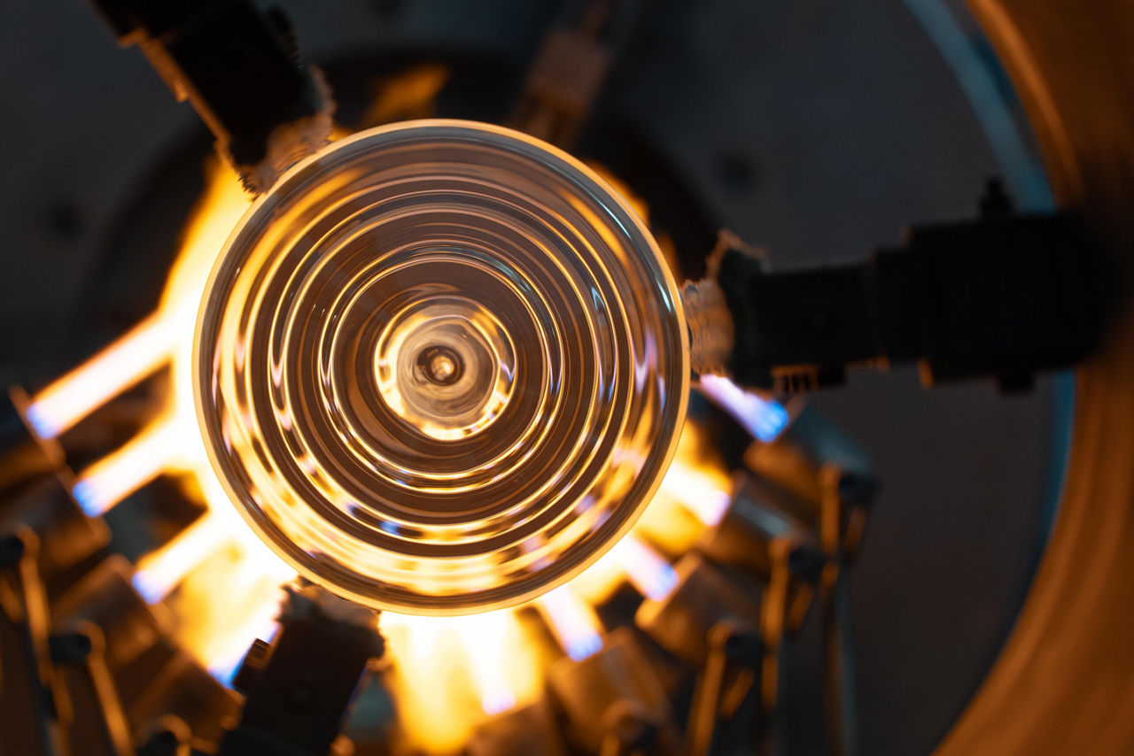 Ein rundes Glasstück, auf das von allen Seiten brennende Gasbrenner einwirken.