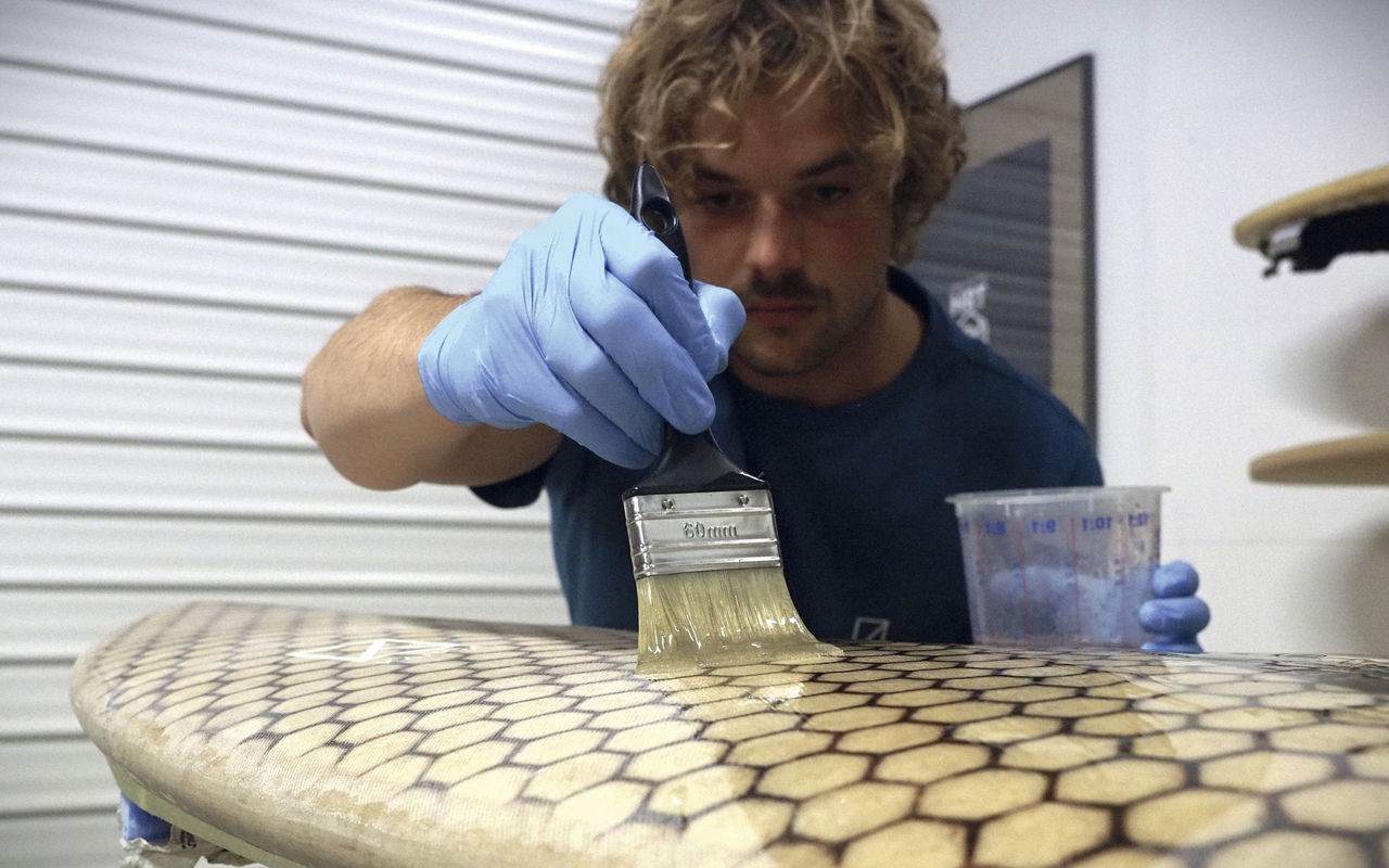 Thilo von Osterhausen runs a brush over the surface of a KANOA surfboard.