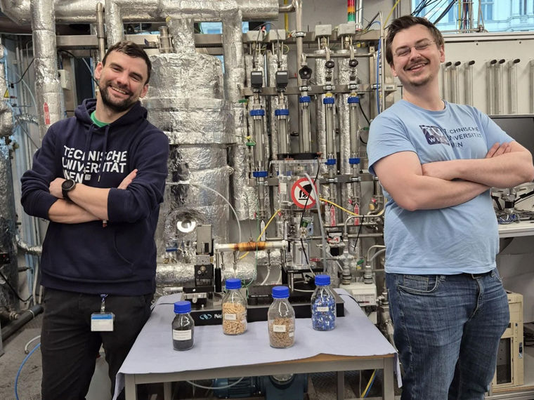 Two scientists stand with their arms crossed next to fabric samples. They are smiling at the camera.