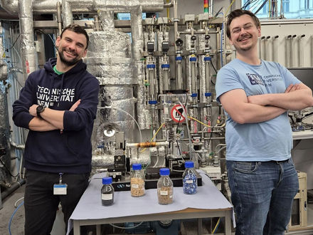 Two scientists stand with their arms crossed next to fabric samples. They are smiling at the camera.