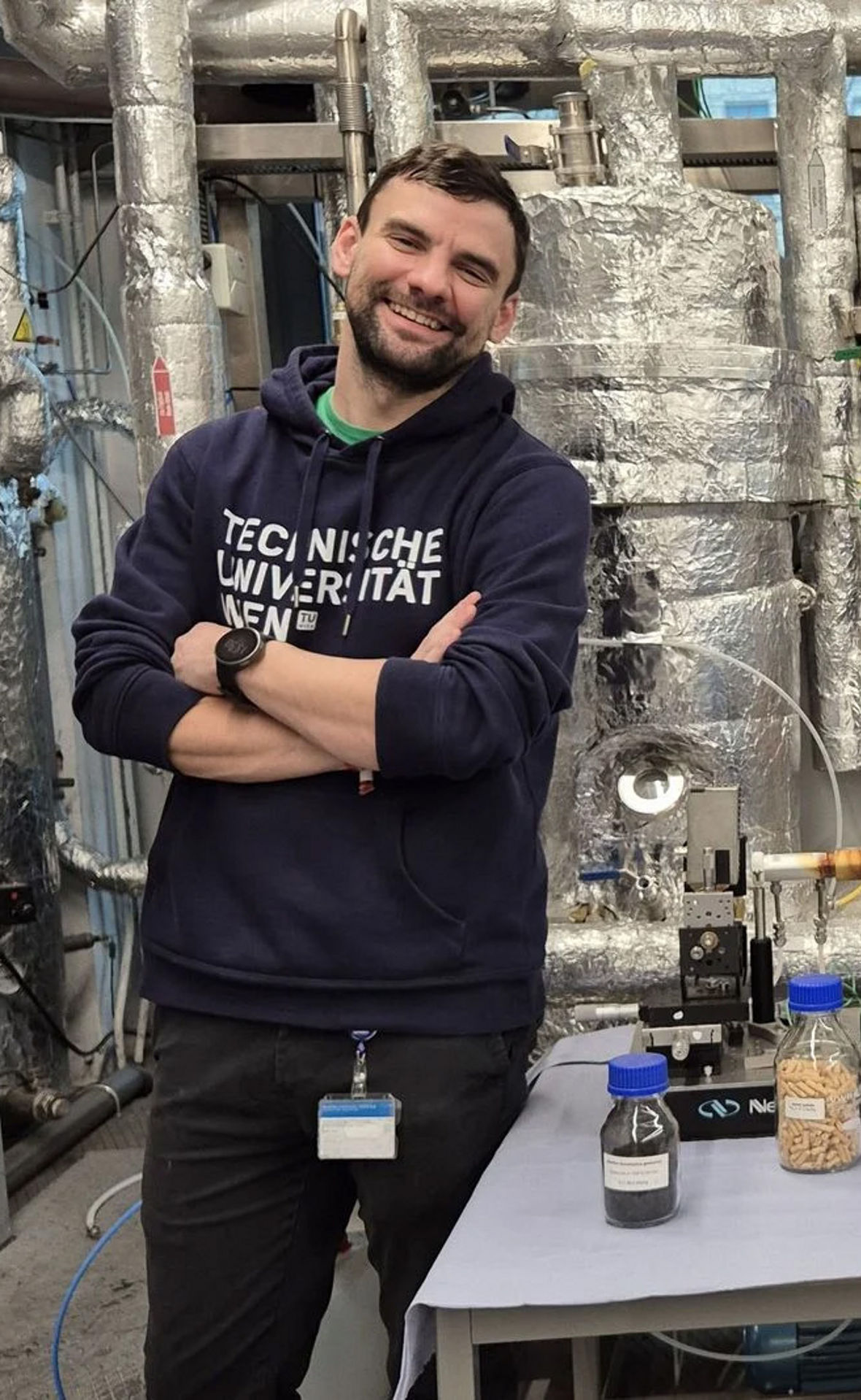 Zwei junge Wissenschaftler stehen mit verschränkten Armen neben Stoffproben. Sie Lachen in die Kamera.