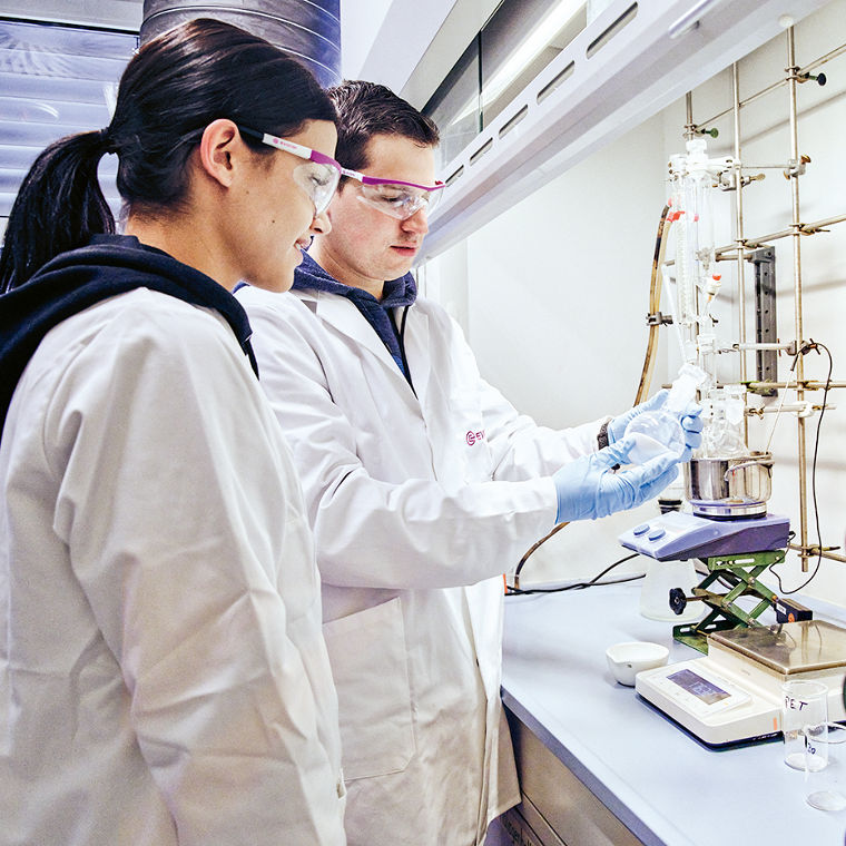 Two lab technicians in white coats are collaborating on an experiment at a laboratory workstation.