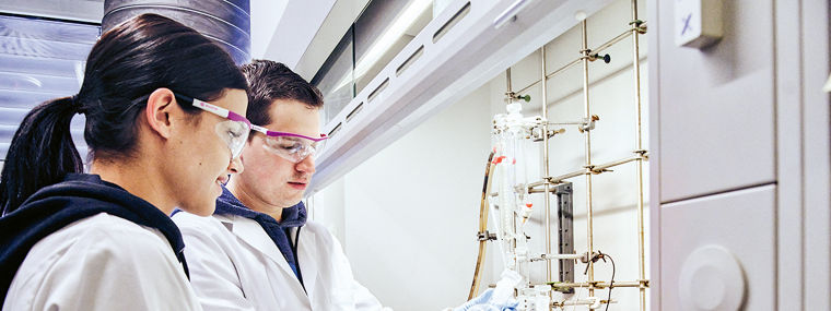 Two lab technicians in white coats are collaborating on an experiment at a laboratory workstation.