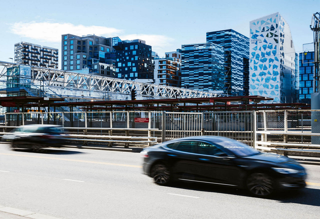 Zwei Autos fahren über eine Straße vor sehr moodernen Hochhäusern.
