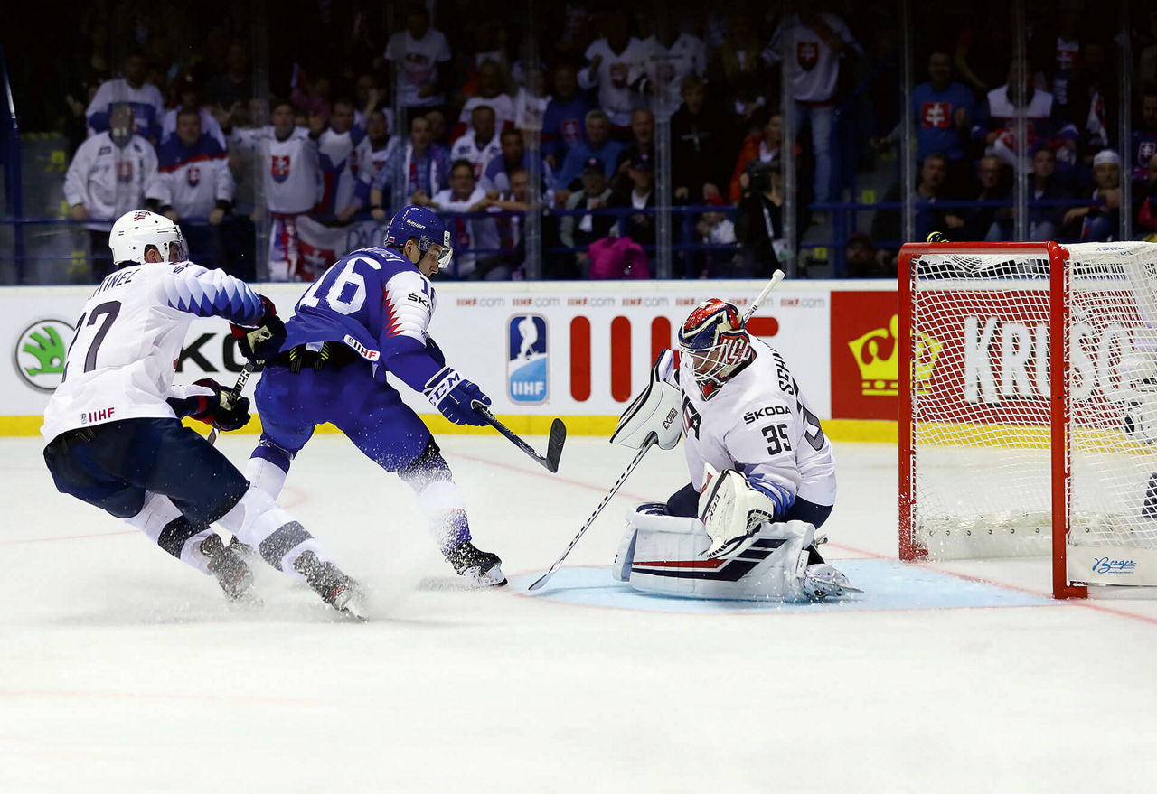 Zwei Eishockeyspieler und der Torwart im Wettkampf um den Puck.