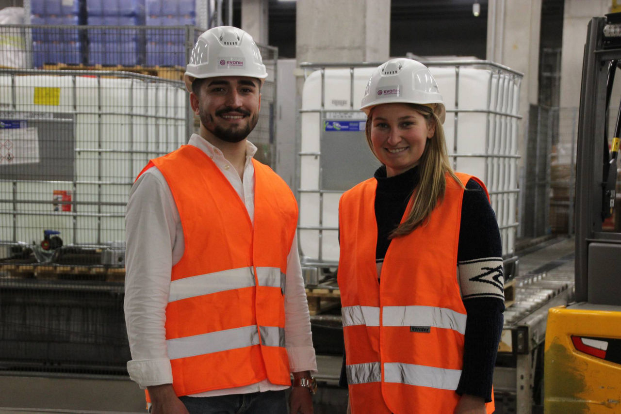 Two employees wearing safety vests and helmets in a warehouse setting.