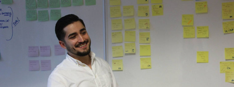 A person stands in front of a whiteboard filled with colorful sticky notes organized into categories for project management.