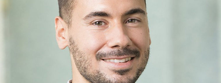 A man wearing a suit and shirt poses in a professional setting.