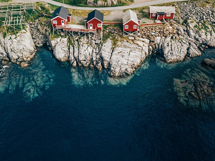 Rote Holzhäuser stehen zum Teil auf hohen Stelzen an der felsigen Klippe eines Fjords.