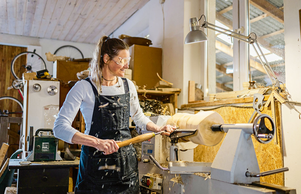 A carpenter is standing at a lathe and working a piece of wood.