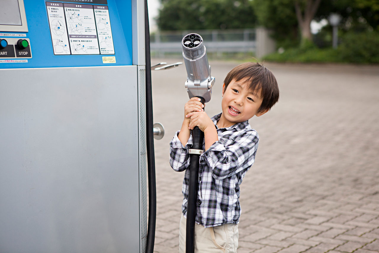 A small boy lifts up a large plug for charging electric cars.