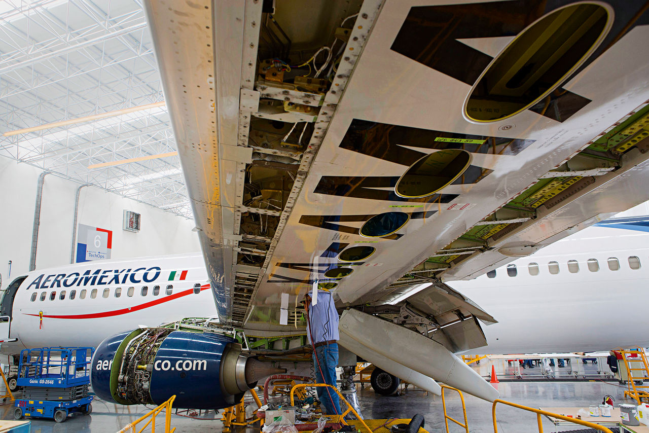 Ein Werkstatt-Mitarbeiter steht unter eineem Flügel eines Flugzeugs der AEROMEXICO. Sein Kopf ist innerhalb des Flügels.