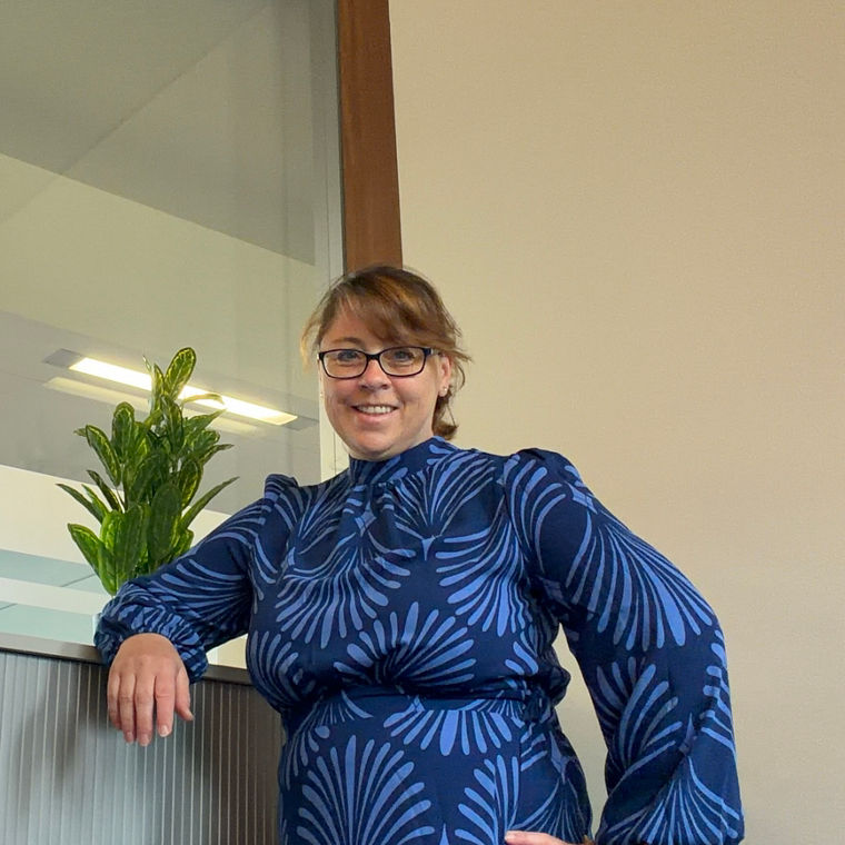Person in a blue patterned dress leaning on a cabinet with a green plant on top.