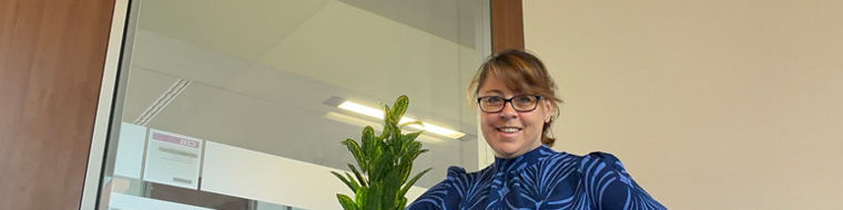 Person in a blue patterned dress leaning on a cabinet with a green plant on top.