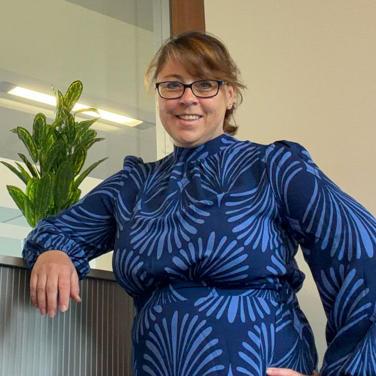 Person in a blue patterned dress leaning on a cabinet with a green plant on top.