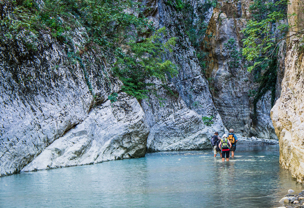 Wanderer waten in einer Felsschlucht durch einen flachen Fluss.