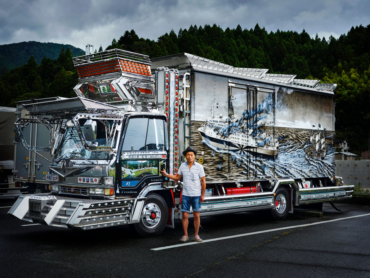 A man with a hat on his head stands in front of a completely painted and heavily modified artistically designed truck.