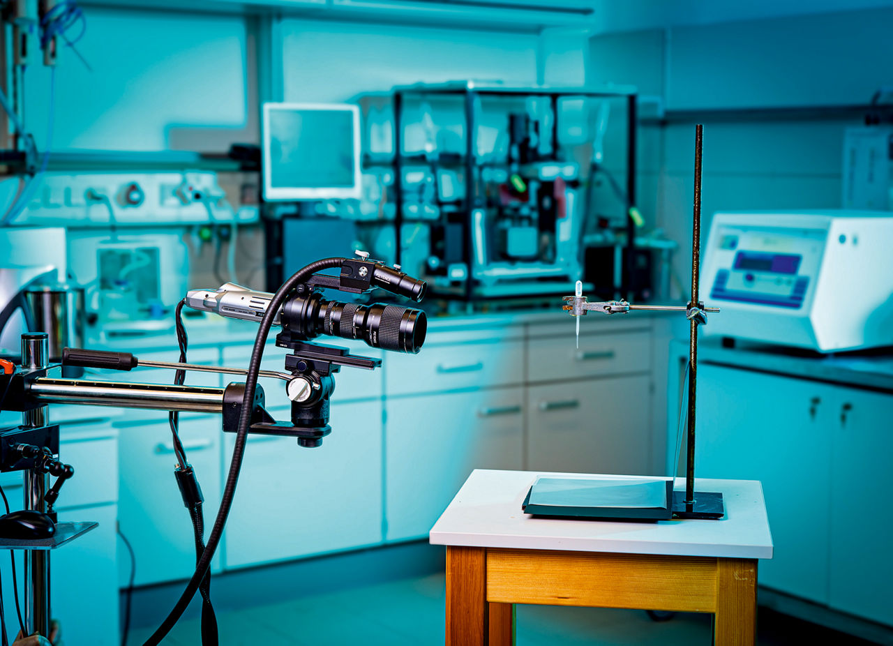 Eine Kamera auf einem Stativ filmt in Richtung eines kleinen Testbehälters, aus dem Tropfen fallen.