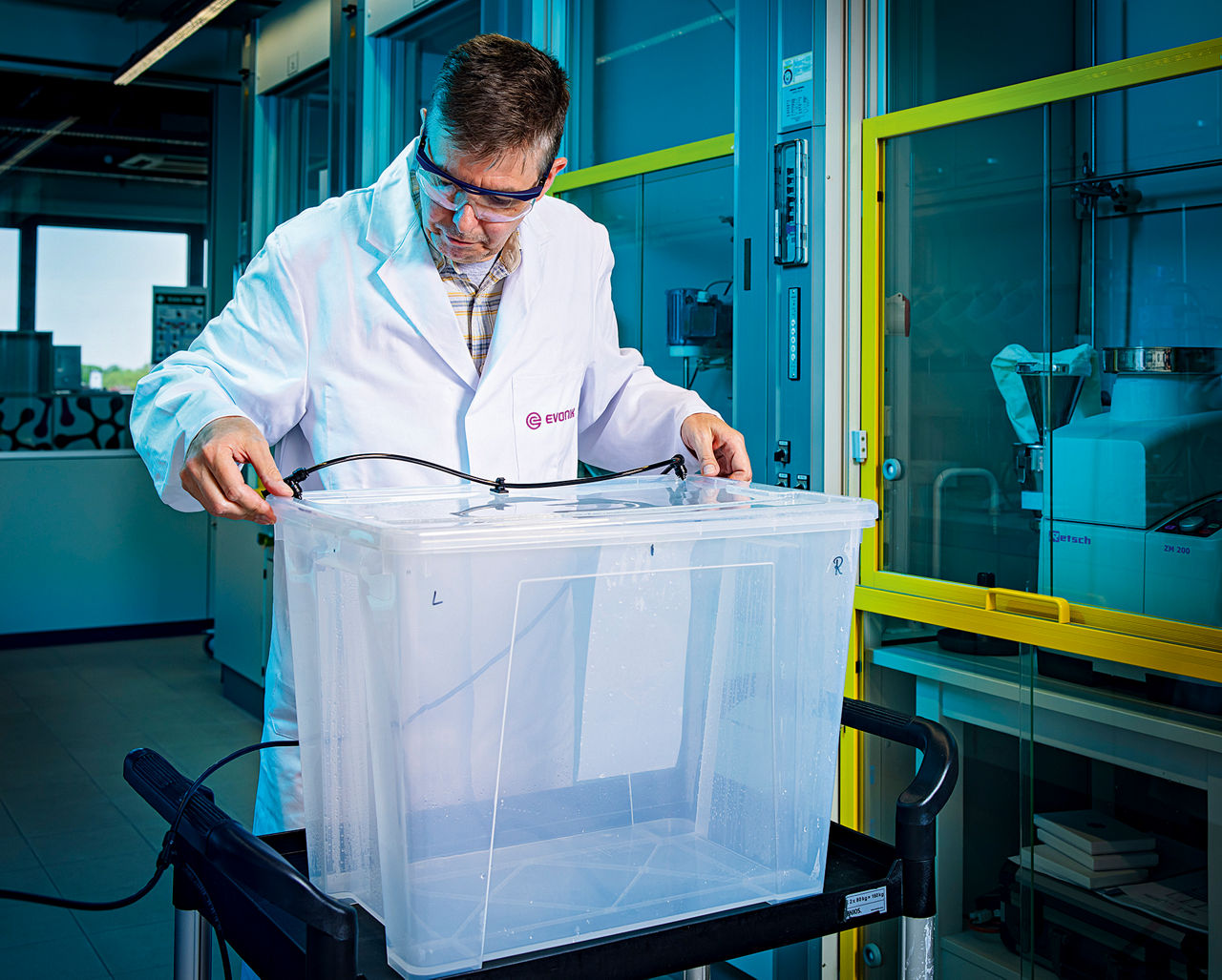 Laborant Volker Klotzbach bereitet eine Box vor, hinter der er steht und einen Schlauch darin befestigt.