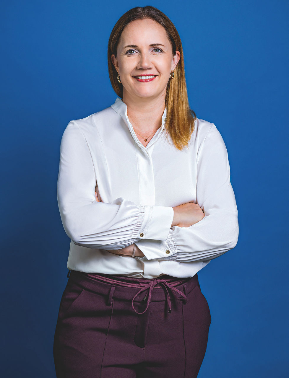 Romy Schnelle steht mit verschränkten Armen vor einem blauen Hintergrund und lächelt in die Kamera.