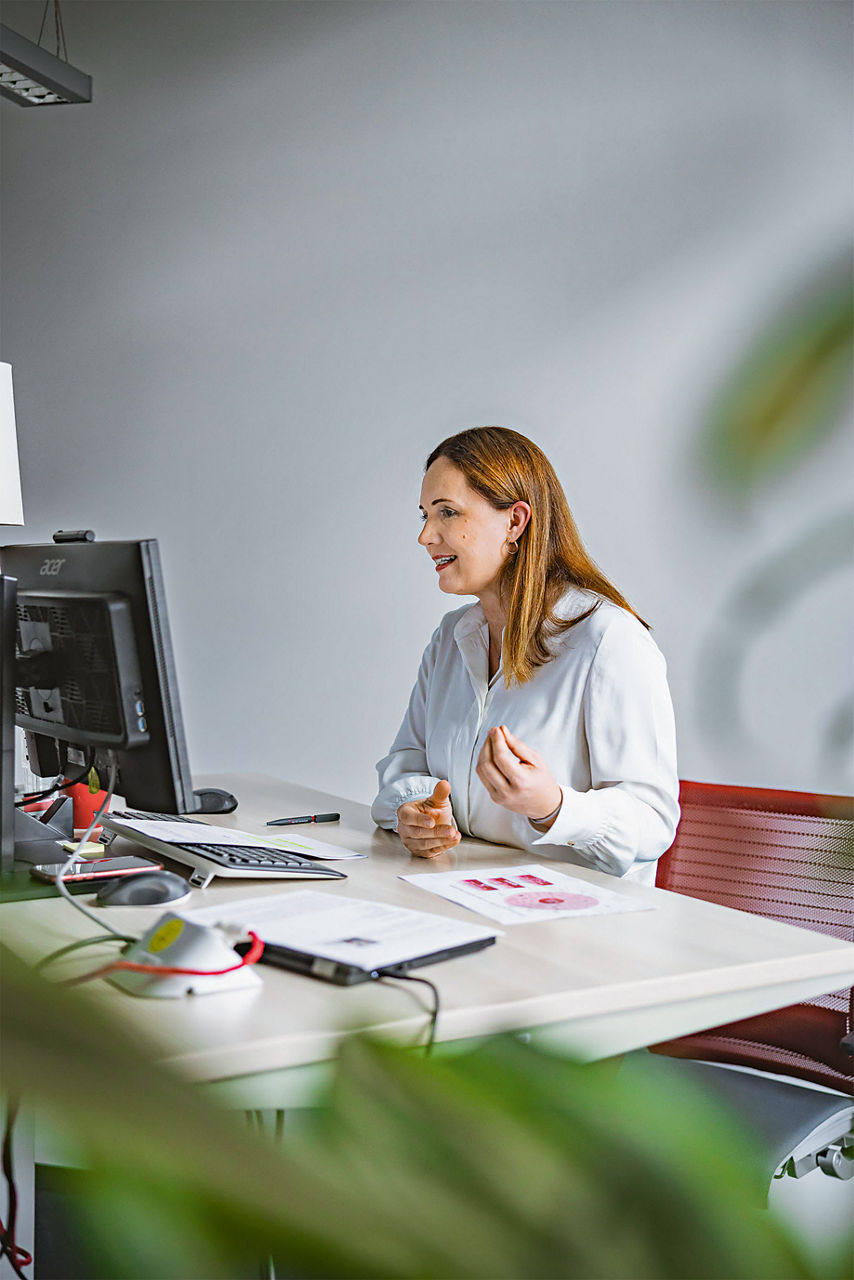 Romy Schnelle an ihrem Schreibtisch, sie gestikuliert mit ihren Händen, während sie an der Videokonferenz teilnimmt.