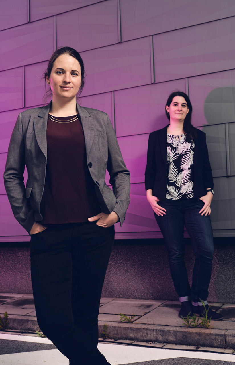  Linda Arsenjuk und Corina Nentwich stehen versetzt vor einer in Deep Purple angestahlten Außenwand im Chemiepark Marl